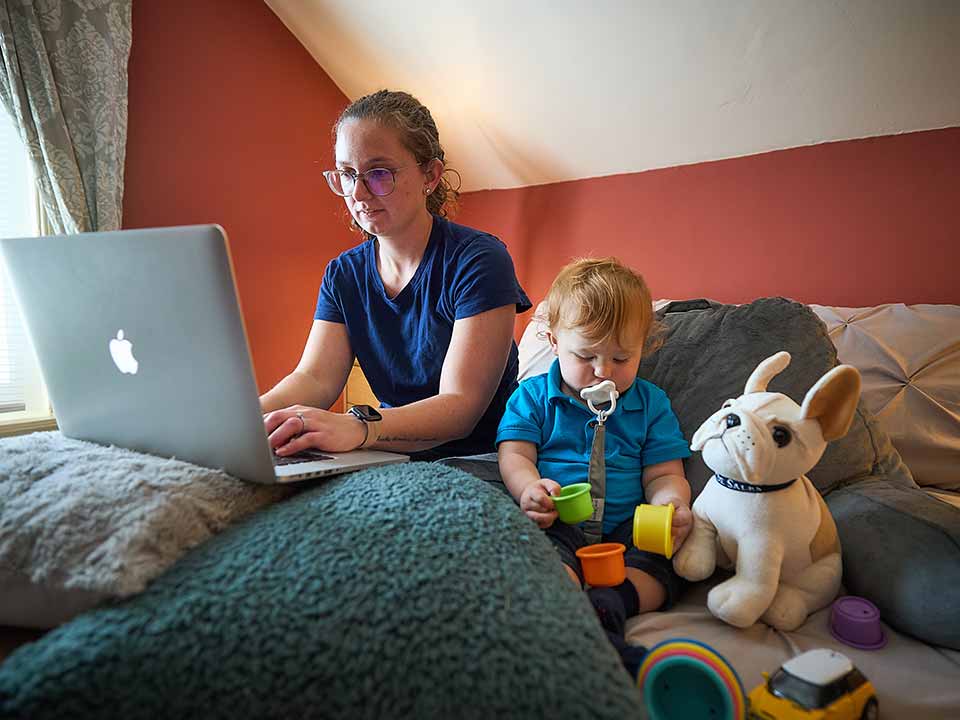 student working on laptop with child on bed