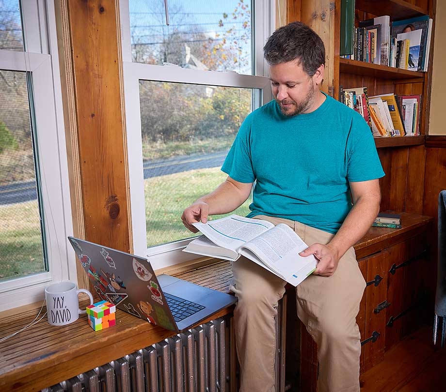male student reading textbook near window